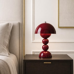 May include: A glossy, deep red table lamp with a spherical base and a half-dome shade. The lamp has a stacked ball design and a chrome accent on top. It sits on a dark brown nightstand, adding a pop of color to the room.