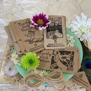May include: A stack of brown cards with black ink illustrations and text. The cards feature a mermaid, a swan, and a woman with a flower. The text on the cards reads "Earthy Soul Resale" and "Follow on Instagram @earthysoulresale".