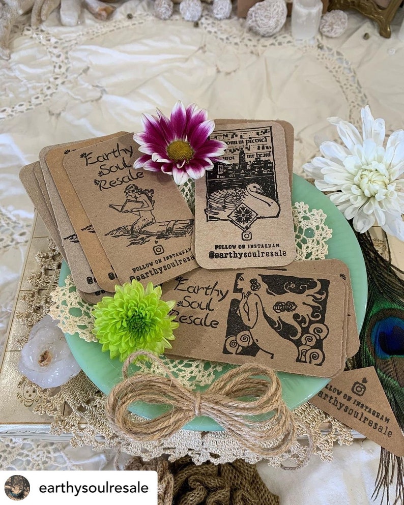 May include: A stack of brown cards with black ink illustrations and text. The cards feature a mermaid, a swan, and a woman with a flower. The text on the cards reads "Earthy Soul Resale" and "Follow on Instagram @earthysoulresale".