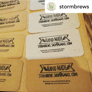 May include: Close-up of several brown paper business cards with the text "HAND MADE" and "STORMBREWS.SHOP@GMAIL.COM" printed in black. The cards also include the social media handles "facebook.com/stormbrews.shop" and "instagram.com/stormbrews".