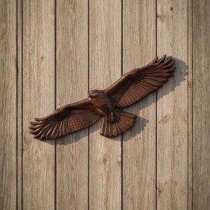 Può includere: Scultura marrone di un falco in volo, montata su una parete di assi di legno. Le ali del falco sono completamente estese, mostrando dettagli di piume. La venatura del legno aggiunge una texture naturale.