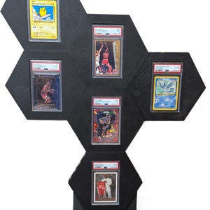 Op de afbeelding: Zwart zeshoekig display met zes beoordeelde ruilkaarten. De kaarten bevatten afbeeldingen van atleten en stripfiguren. Het display is ontworpen om verzamelkaarten te presenteren.