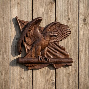 Könnte beinhalten: Detaillierte Holzschnitzerei eines Adlers mit ausgebreiteten Flügeln, der über einer Flagge sitzt. Der Adler ist braun, mit komplizierten Federdetails. Die Flagge hat Sterne und Streifen. Die Schnitzerei ist auf einem Holzgrund montiert.