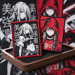 以下が含まれることがあります： アニメスタイルのイラストが描かれた長方形のパッチが2つ。1つは、赤いフレームの中に日本語のテキストが入った女性の白黒画像です。もう1つは、フード付きの人物と日本語のテキストが入った赤いパッチです。どちらも木製のトレイにあります。