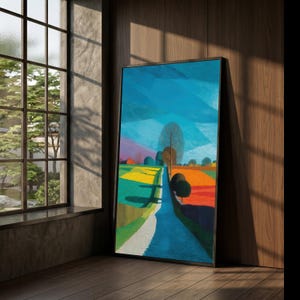 May include: A framed landscape painting with a road winding through colorful fields under a blue sky. The artwork features vibrant hues of yellow, green, orange, and blue, creating a striking visual contrast. The painting is leaning against a wooden wall.