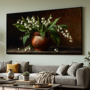 Puede incluir: Impresión en lienzo enmarcada que presenta un bodegón de flores de lirios de los valles en un jarrón de tono cobrizo. La obra de arte muestra flores blancas en forma de campana con hojas verdes, sobre un fondo oscuro y texturizado. El jarrón tiene un aspecto rústico y envejecido.