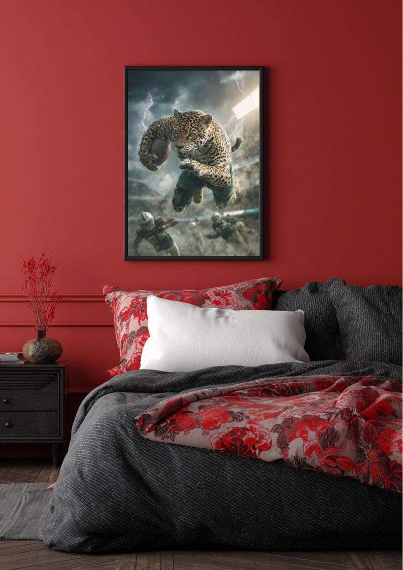 May include: Framed artwork depicting a jaguar playing American football. The image shows the jaguar mid-air, holding the ball, with a stadium and lightning in the background. The artwork hangs above a bed with red and grey bedding.