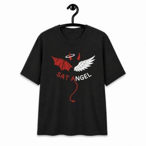 Op de afbeelding: Een zwart t-shirt met korte mouwen en een grafisch ontwerp met een rode duivelvleugel en een witte engelvleugel. Boven de vleugels bevinden zich een rode duivelshoorn en een witte halo. De tekst SAT ANGEL is in rood en wit gedrukt met een rode duivelstaart eronder.