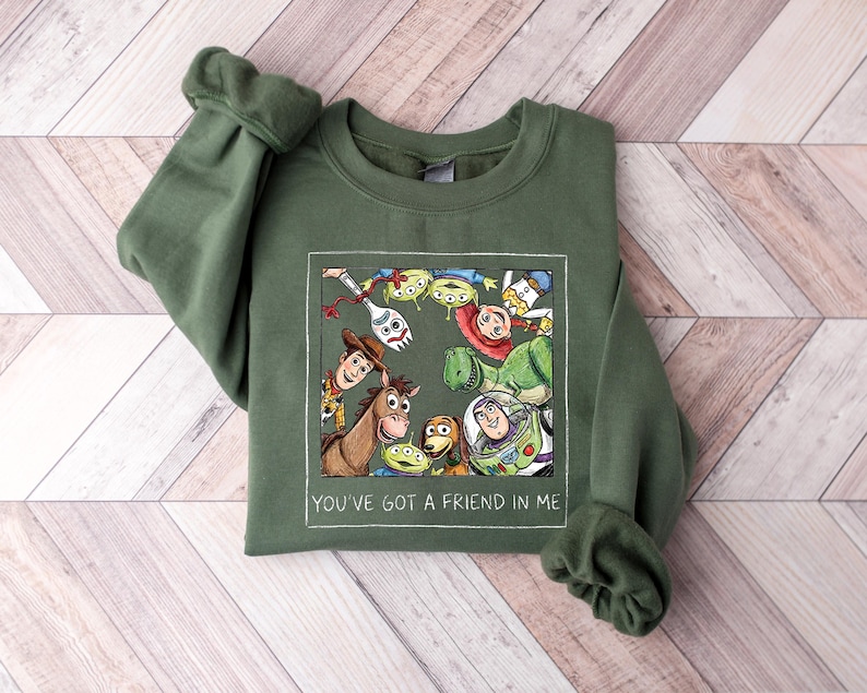 Pu&ograve; includere: Felpa verde oliva con una grafica incorniciata dei personaggi di Toy Story, tra cui Woody e Buzz Lightyear. Il testo "YOU'VE GOT A FRIEND IN ME" &egrave; stampato in bianco sotto. La felpa ha i polsini.
