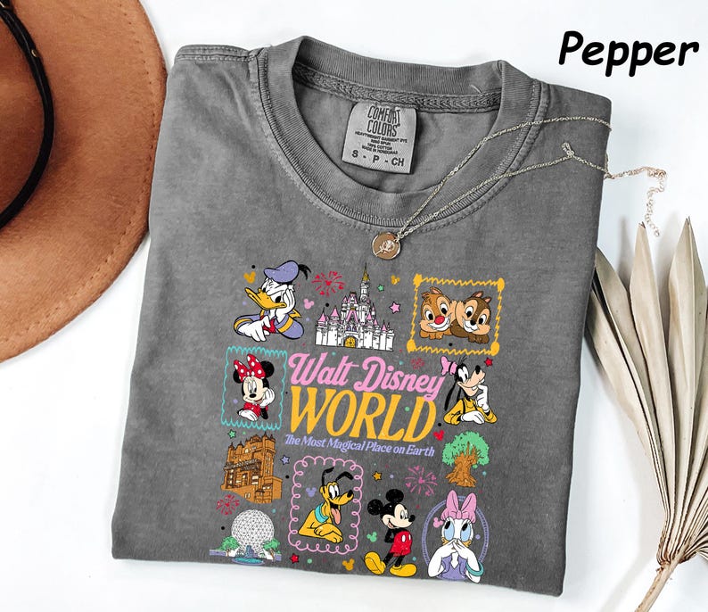 K&ouml;nnte beinhalten: Graues T-Shirt in der Farbe Pfeffer mit einem farbenfrohen Disney-Motiv, das Donald Duck und Mickey Mouse zeigt, sowie dem Text "Walt Disney World". Das T-Shirt hat einen Rundhalsausschnitt.