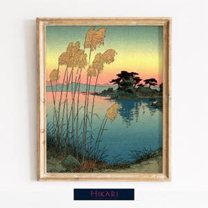 May include: A framed art print depicting a Japanese landscape. Reeds are in the foreground, with a lake and distant shore under a sunset sky. The artwork is in a wooden frame, with the word "Hikari" at the bottom.