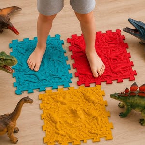 May include: Three square interlocking floor mats in blue, red, and yellow, each featuring embossed dinosaur motifs and the text Littleer.com. The mats are surrounded by various plastic dinosaur figures, including a pterosaur and a stegosaurus.