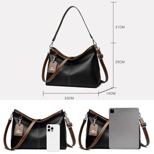Pu&ograve; includere: Borsa a tracolla nera con finiture e cinturini marroni. La borsa &egrave; larga 33 cm, alta 25 cm e profonda 14 cm. Ha una tracolla lunga e un manico pi&ugrave; piccolo. Una piccola etichetta pende dalla tracolla.