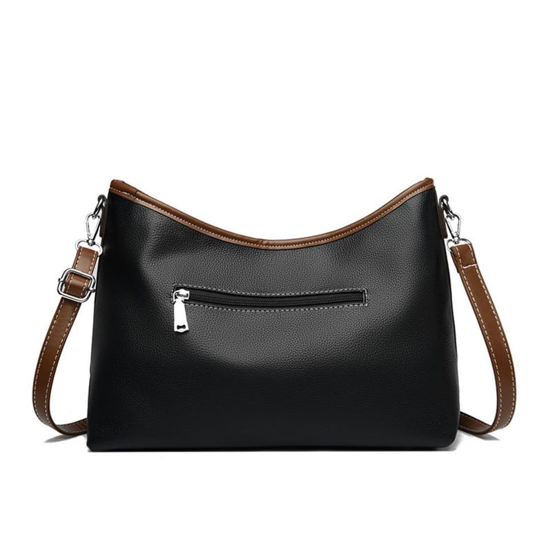 Pu&ograve; includere: Borsa a tracolla nera con finiture e cinturino marroni. La borsa ha una chiusura a cerniera sul retro e una chiusura in metallo color argento. La borsa &egrave; realizzata in un materiale liscio simile alla pelle.