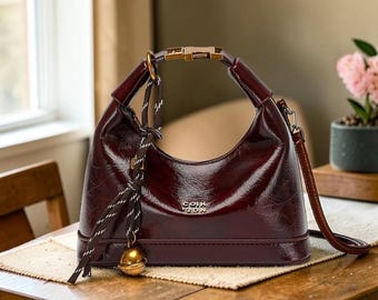 Borsa a tracolla Hobo in ecopelle testurizzata color bordeaux con ciondolo a nappa e forma a mezzaluna.