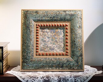 May include: A square picture frame with a textured, mottled teal and gold finish. The inner border features a row of small, rounded, reddish-orange beads. The centre displays a square panel with a light-coloured floral pattern in blue and gold tones.
