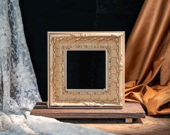 May include: A square picture frame with a metallic gold finish and a textured, repeating scalloped pattern along the border. The frame features a deep, recessed centre with a black interior, providing a high-contrast look for display purposes.