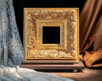 May include: A square picture frame with a metallic gold finish, featuring intricate relief carvings of scrolling foliage and floral patterns. The frame has a deep, multi-layered profile with a central square opening and a dark, recessed inner border.