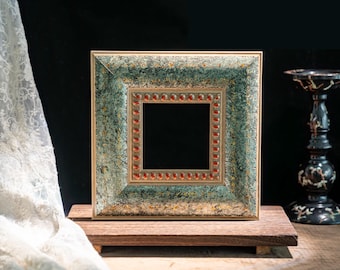 May include: A square picture frame featuring a textured, mottled teal and gold finish. The inner border is decorated with a repeating pattern of small, raised, reddish-brown oval accents set against a metallic gold trim, creating a detailed frame.