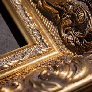 May include: A gold-colored picture frame featuring intricate, raised relief carvings and a textured, cross-hatched pattern. The frame has a dark, recessed finish within the decorative grooves, highlighting the metallic gold surface details.