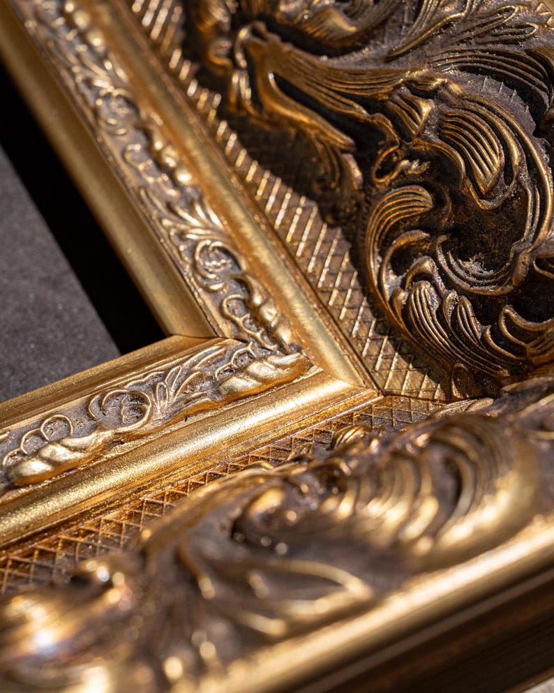 May include: A gold-colored picture frame featuring intricate, raised relief carvings and a textured, cross-hatched pattern. The frame has a dark, recessed finish within the decorative grooves, highlighting the metallic gold surface details.