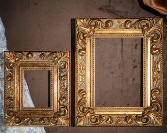 May include: Two rectangular picture frames with ornate, raised scrollwork and leaf motifs. The frames feature a metallic gold finish with distressed, muted green undertones, showcasing a beaded inner border and a wide, decorative outer edge.