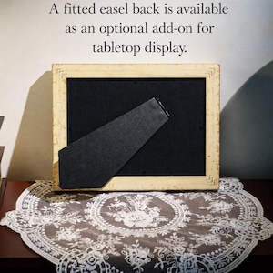 May include: A rectangular picture frame with a distressed cream-colored finish and a black backing featuring a hinged easel stand. The text above the frame reads: A fitted easel back is available as an optional add-on for tabletop display.