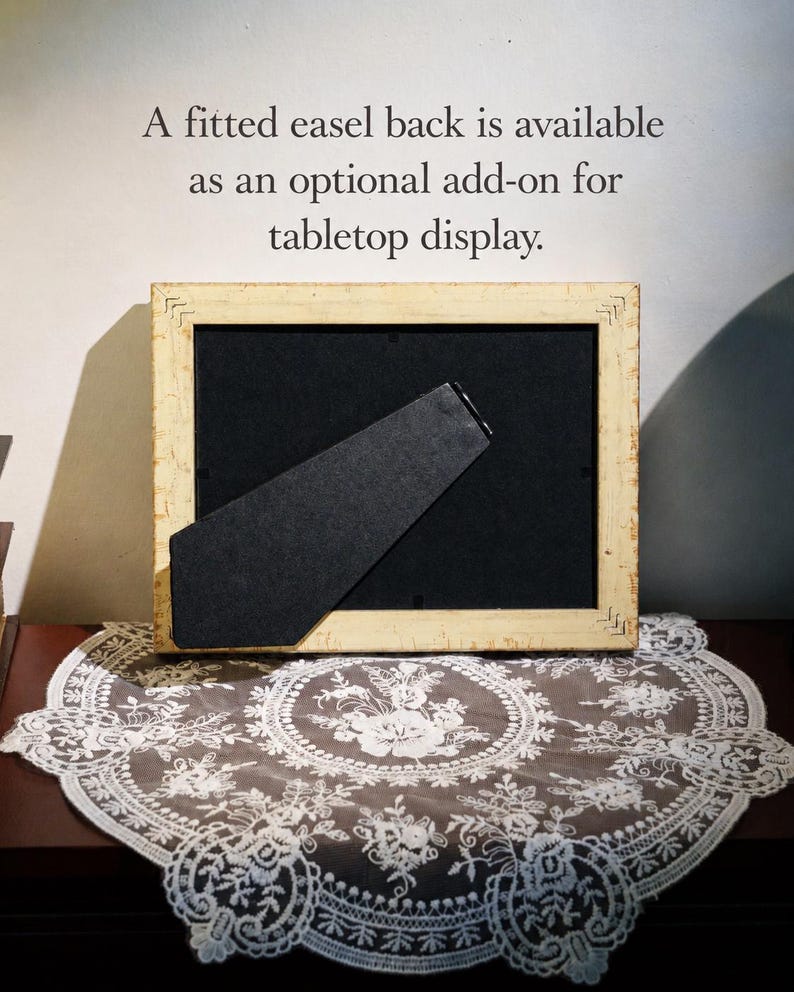 May include: A rectangular picture frame with a distressed cream-colored finish and a black backing featuring a hinged easel stand. The text above the frame reads: A fitted easel back is available as an optional add-on for tabletop display.