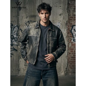 Könnte beinhalten: Eine schwarze Lederjacke im Used-Look mit klassischem Kragen, langen Ärmeln und Frontreißverschluss, getragen über einem schlichten dunkelgrauen T-Shirt und einer dunkelblauen Jeans. Die Jacke hat eine abgenutzte Textur und sichtbare Nähte.