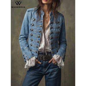 May include: A blue denim military-style jacket featuring rows of metallic buttons, a structured collar, and long sleeves with ruffled white cuffs. The jacket is worn over a white shirt, paired with blue denim jeans featuring a black leather belt.
