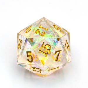 Könnte beinhalten: Ein klarer, schillernder zwanzigseitiger Würfel mit goldfarbenen Zahlen. Der Würfel ist facettiert, wobei jede Seite eine andere Zahl anzeigt. Der Gesamteffekt ist ein schimmerndes, edelsteinartiges Aussehen, ideal für Tabletop-Spiele.