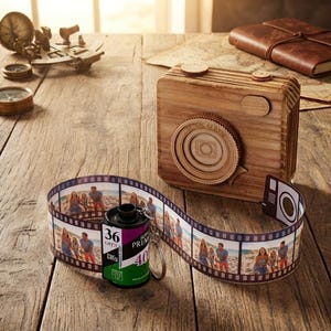 May include: A wooden camera model with a circular lens and two top buttons, paired with a black film canister keychain attached to a long strip of photographic film featuring multiple color images of people on a beach.