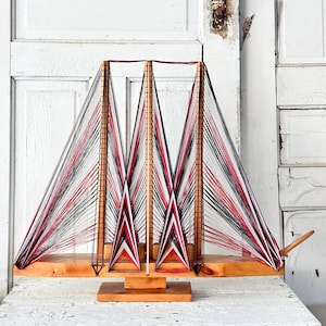 May include: A wooden sailboat model with red, white, and black string sails. The sails are woven in a geometric pattern.