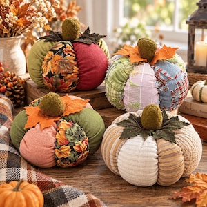 May include: Four fabric pumpkins featuring various textures and patterns, including autumn leaf prints, solid green, red, and striped corduroy sections. Each pumpkin is topped with a small, textured green stem and fabric leaves.