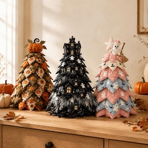 May include: Three decorative fabric trees for Halloween. The left tree features orange and green pumpkin patterns with a pumpkin topper. The center tree is black with a haunted house and ghost motifs. The right tree is pink and blue with ghosts.