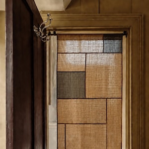 May include: A rectangular door curtain made of textured, woven fabric featuring a geometric patchwork design. The curtain consists of various tan, beige, and dark gray rectangular panels separated by thin, dark brown stitched lines.