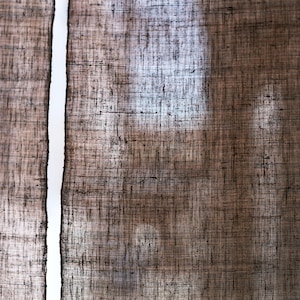 Puede incluir: Un par de cortinas marrones semitransparentes con una textura tejida gruesa y visible. La tela muestra un tono marr&oacute;n tierra oscuro con variaciones sutiles en el tejido, permitiendo que la luz pase a trav&eacute;s de los espacios en las fibras.