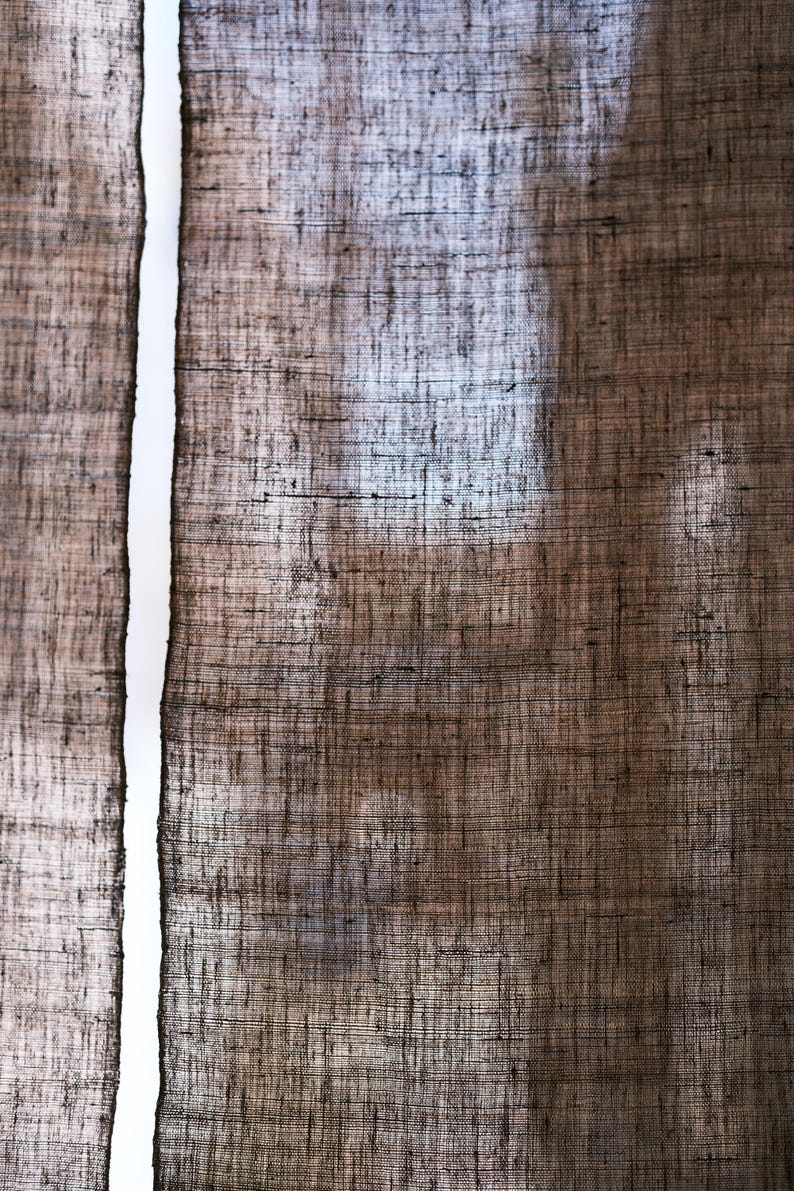 Puede incluir: Un par de cortinas marrones semitransparentes con una textura tejida gruesa y visible. La tela muestra un tono marr&oacute;n tierra oscuro con variaciones sutiles en el tejido, permitiendo que la luz pase a trav&eacute;s de los espacios en las fibras.