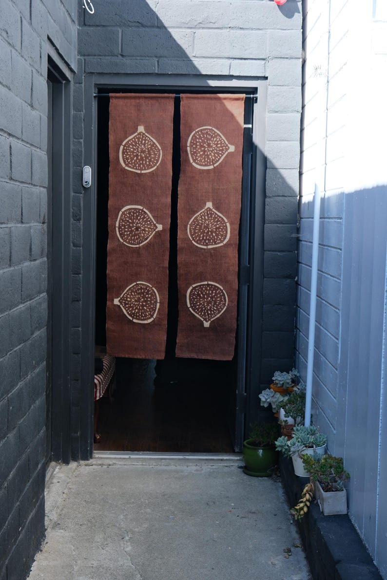 Puede incluir: Una cortina de puerta de tela marr&oacute;n de dos paneles con un patr&oacute;n repetitivo de higos en color crema. La cortina cuelga de una barra negra en el marco de una puerta, mostrando tres ilustraciones verticales de higos en cada panel.