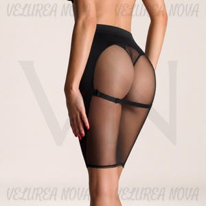 Peut inclure: Une jupe noire dotée d'une bande opaque à taille haute et d'un panneau arrière en maille transparente. Le vêtement comprend une sangle noire horizontale au niveau de la mi-cuisse, reliant les côtés de la jupe. Le texte VELUREA NOVA est visible.