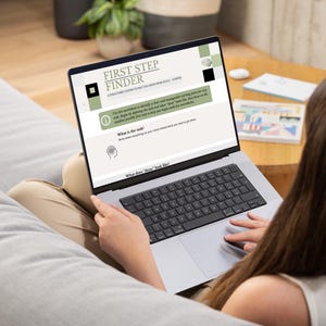 Peut inclure: Un ordinateur portable affiche "FIRST STEP FINDER" sur son écran. L'écran présente un design vert et blanc avec du texte et des graphiques. L'ordinateur est posé sur les genoux d'une personne assise sur un canapé gris.