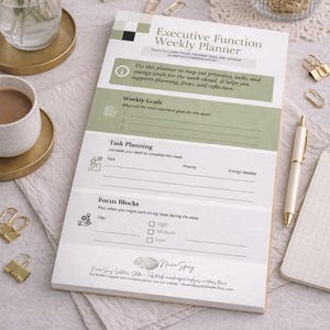 May include: Executive Function Weekly Planner with sections for weekly goals, task planning, and focus blocks. The planner is white with green accents and includes the text "Executive Function Weekly Planner". A pen, notepad, and gold binder clips are also visible.