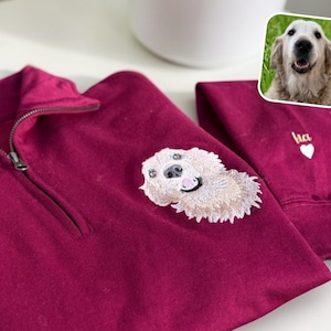 Könnte beinhalten: Burgunderfarbenes Sweatshirt mit kurzem Reißverschluss und einem bestickten Hundepatch. Der Hund ist beige und lächelt. Auf dem Ärmel sind ein kleines Herz und der Name "lia" gestickt.