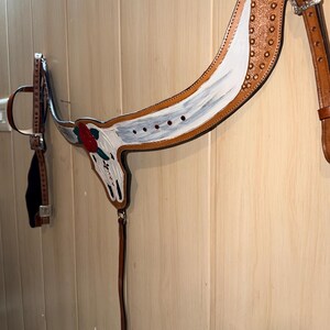 Puede incluir: Un petral de cuero color canela para caballo con un dise&ntilde;o pintado a mano de un cr&aacute;neo de toro blanco y una rosa roja. La pieza incluye hebillas de metal plateado, tachuelas decorativas color cobre y correas de cuero ajustables.