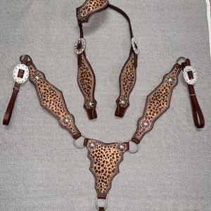 Puede incluir: Un juego completo de guarniciones para caballos con un diseño de estampado de leopardo. El juego incluye un cabezal, un peto y riendas. La guarnición es marrón con detalles plateados y pedrería decorativa.