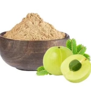 Puede incluir: Un cuenco de madera lleno de polvo marrón claro se encuentra junto a una fruta verde entera y otra cortada por la mitad, con hojas verdes. La fruta es redonda y tiene una piel lisa. El polvo parece finamente molido.