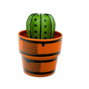 May include: A green cactus with black dots sits in an orange pot with black dotted and striped details. The pot has a round shape and is made of a hard material. The cactus is a decorative item.
