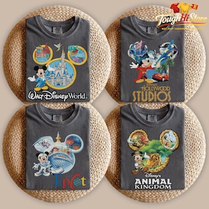 May include: Four gray t-shirts with Disney theme park designs. Each shirt features a Mickey Mouse head outline with park-specific graphics and text: "Walt Disney World," "Hollywood Studios," "Epcot," and "Animal Kingdom."