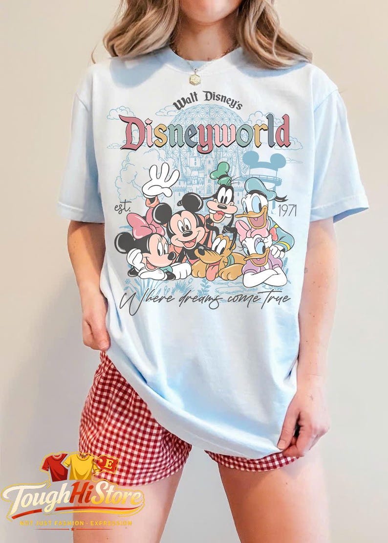 Puede incluir: Camiseta azul claro con un dise&ntilde;o de Disney con Mickey y Minnie Mouse, Goofy y Donald y Daisy Duck. La camiseta tiene el texto "Walt Disney's Disneyworld est. 1971" y "Where dreams come true."