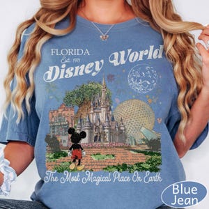 K&ouml;nnte beinhalten: Ein blaues T-Shirt mit einem Grafikdruck von Florida Disney World, einschlie&szlig;lich Schloss, Epcot-Sph&auml;re, Hollywood Tower Hotel und Mickey Mouse. Der Text lautet Florida Est. 1971, Disney World und The Most Magical Place On Earth.